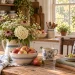 Rustic farmhouse kitchen with fresh flowers, a bowl of apples, vintage dishes, and a coffee mug on a wooden table.